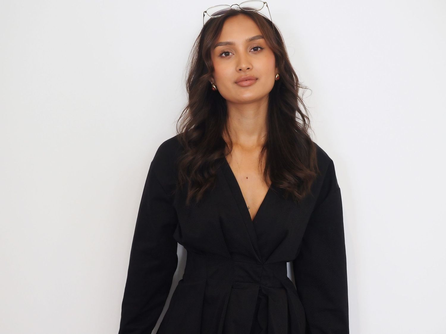 A woman in a white off-shoulder top poses against a light background with soft natural lighting.