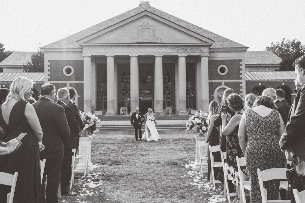 A black and white wedding ceremony taking place in front of a grand neoclassical building with columns.