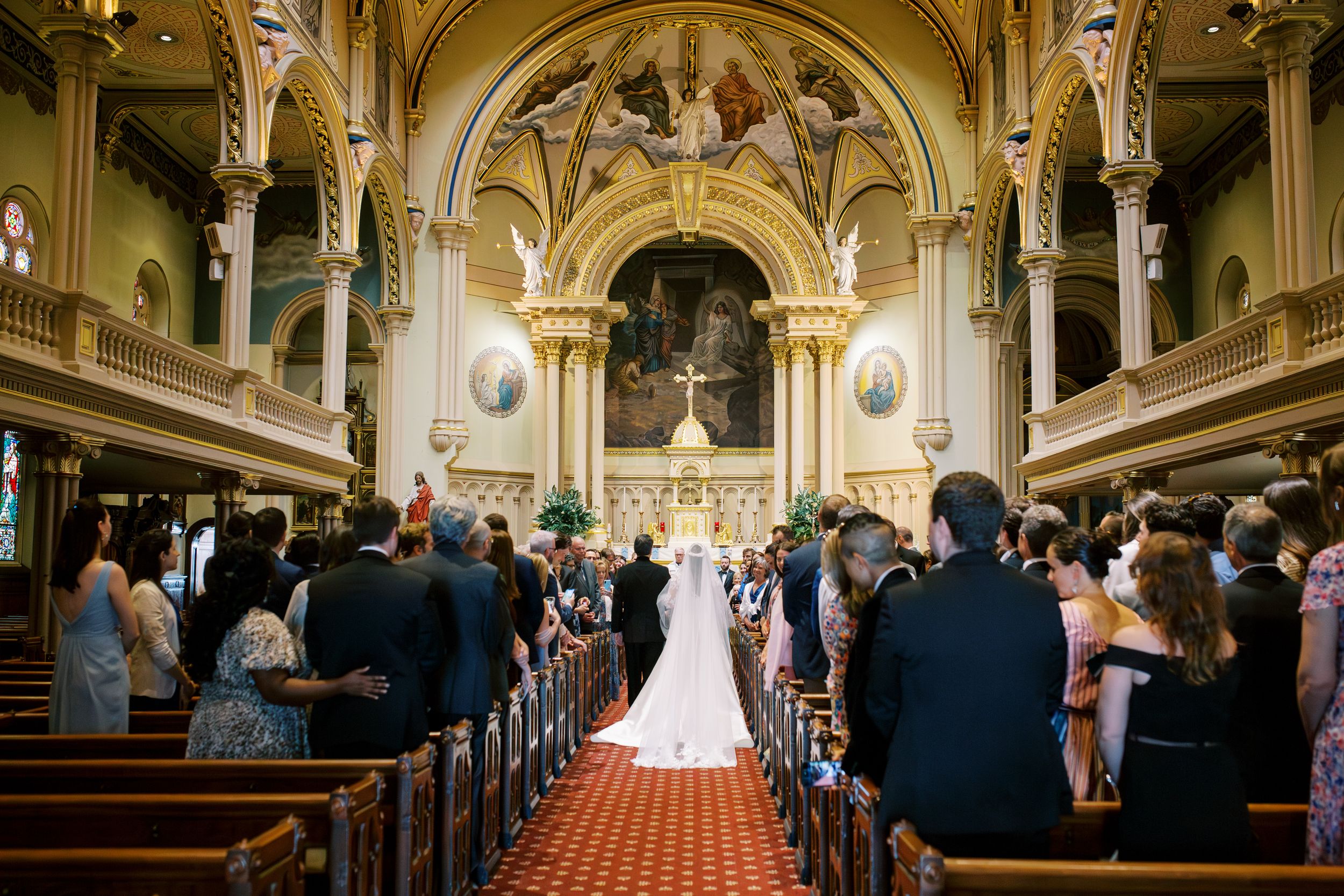 A traditional church wedding ceremony takes place in an ornate cathedral with vaulted ceilings and stained glass windows.