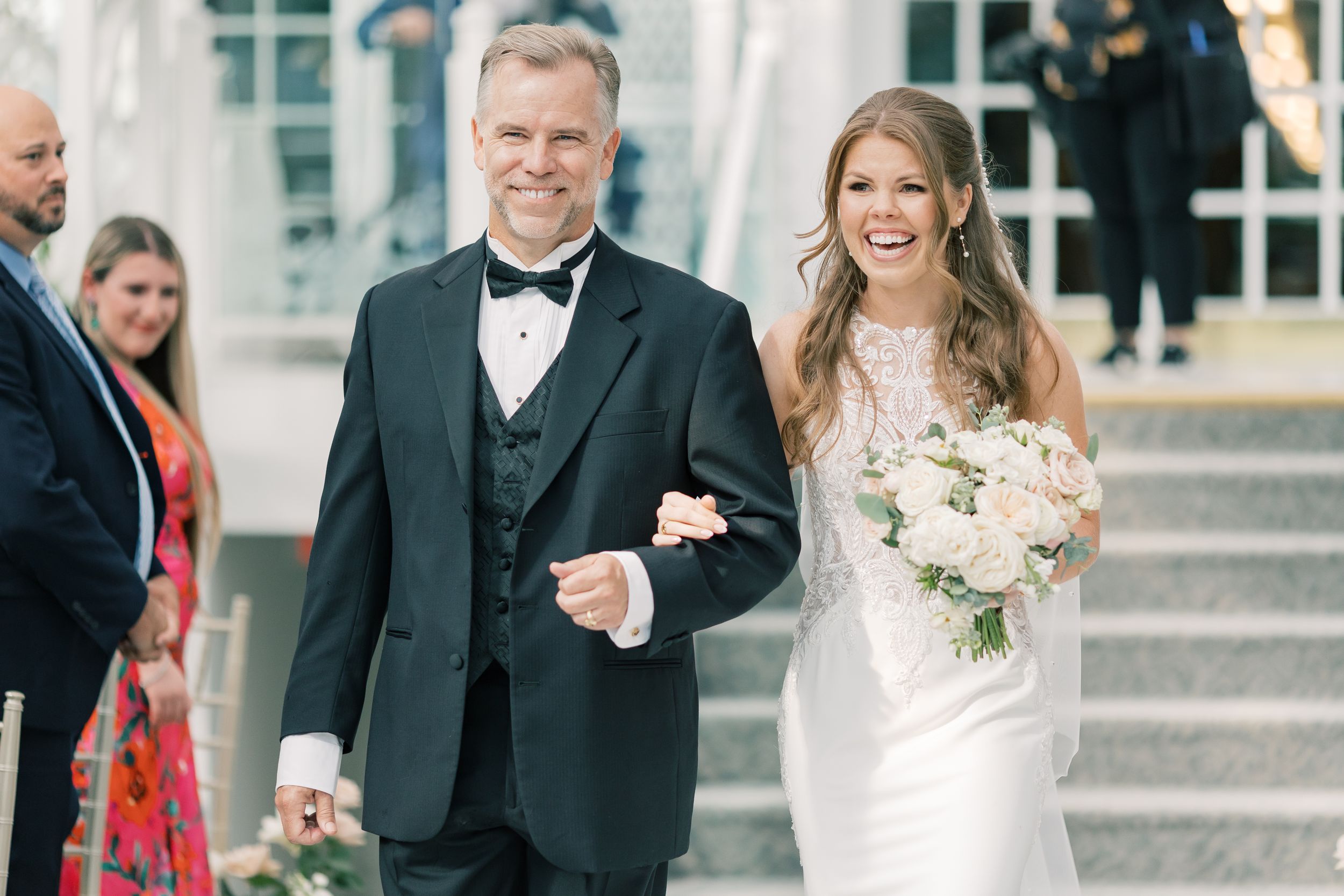A joyful wedding moment captured as couple walks together with flowers and formal attire down outdoor steps.