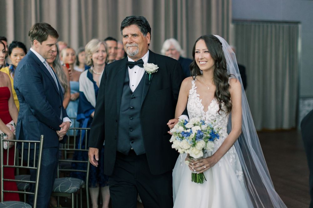 A happy moment during a formal wedding ceremony as the bride in a white dress holds a blue and white bouquet.