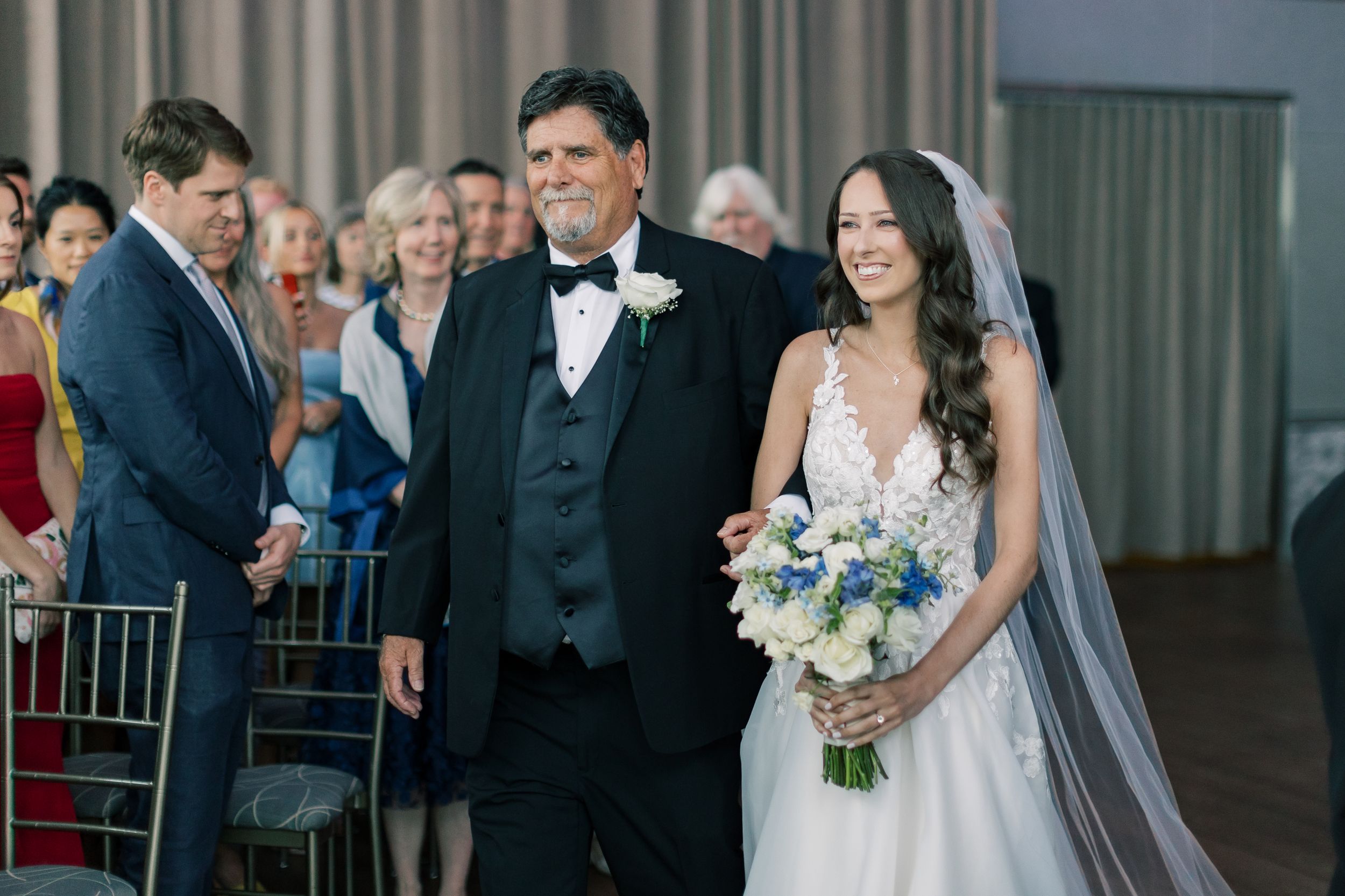 A happy moment during a formal wedding ceremony as the bride in a white dress holds a blue and white bouquet.