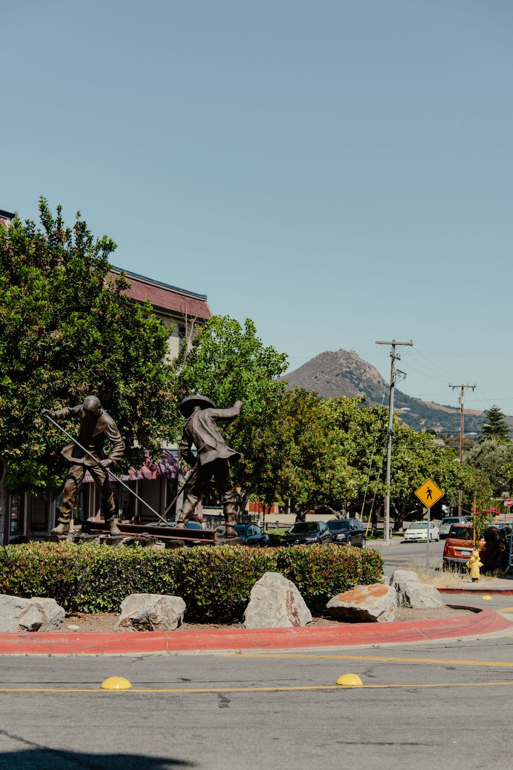 A sculpture display near a street corner with trees and mountains in the background under blue sky.