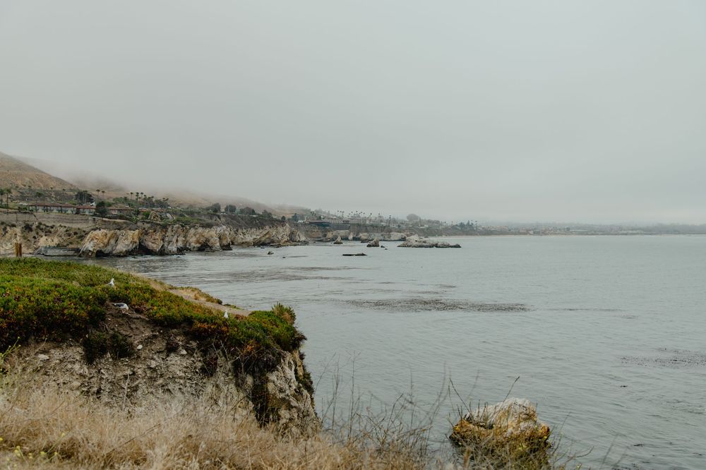 Coastal shoreline with rugged cliffs and misty atmosphere overlooking a gray ocean on an overcast day.