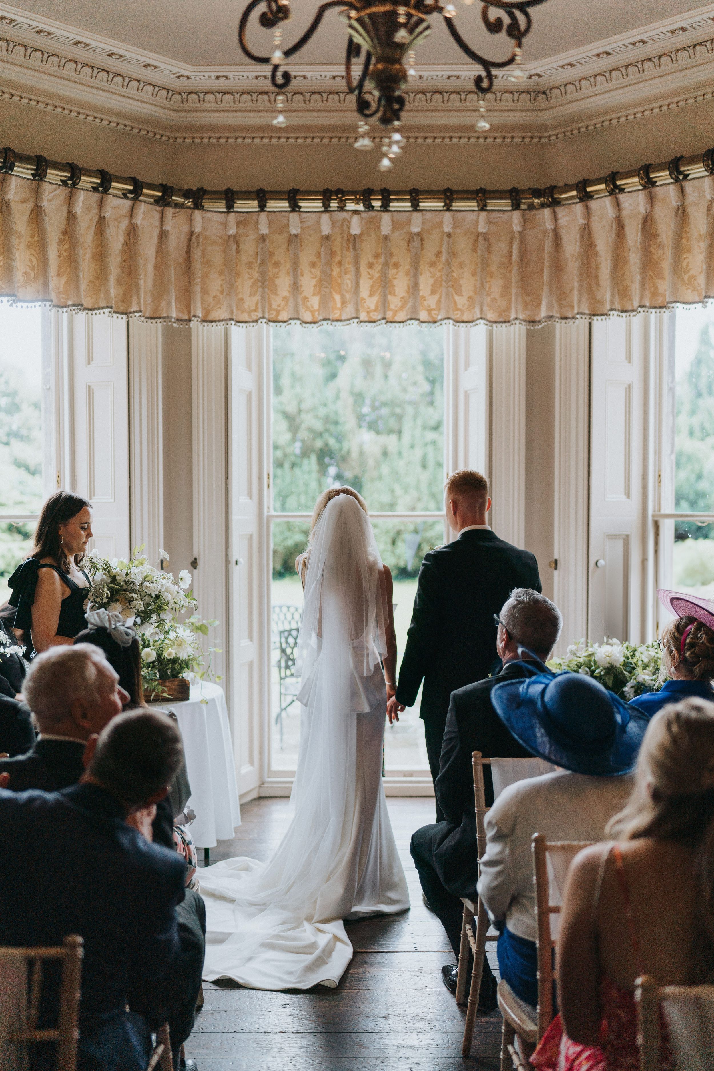 A wedding ceremony in progress inside an elegant white room at Cleatham Hall.