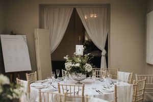 Elegant all-white wedding reception tables with chiavari chairs and draping curtains in a neutral-toned dining room at Cleatham Hall.