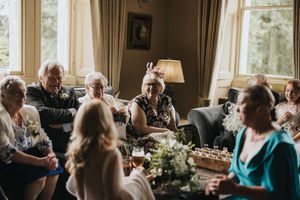 Wedding guests gather in a cosy living room for conversation around floral centrepieces near sunlit windows at Cleatham Hall.