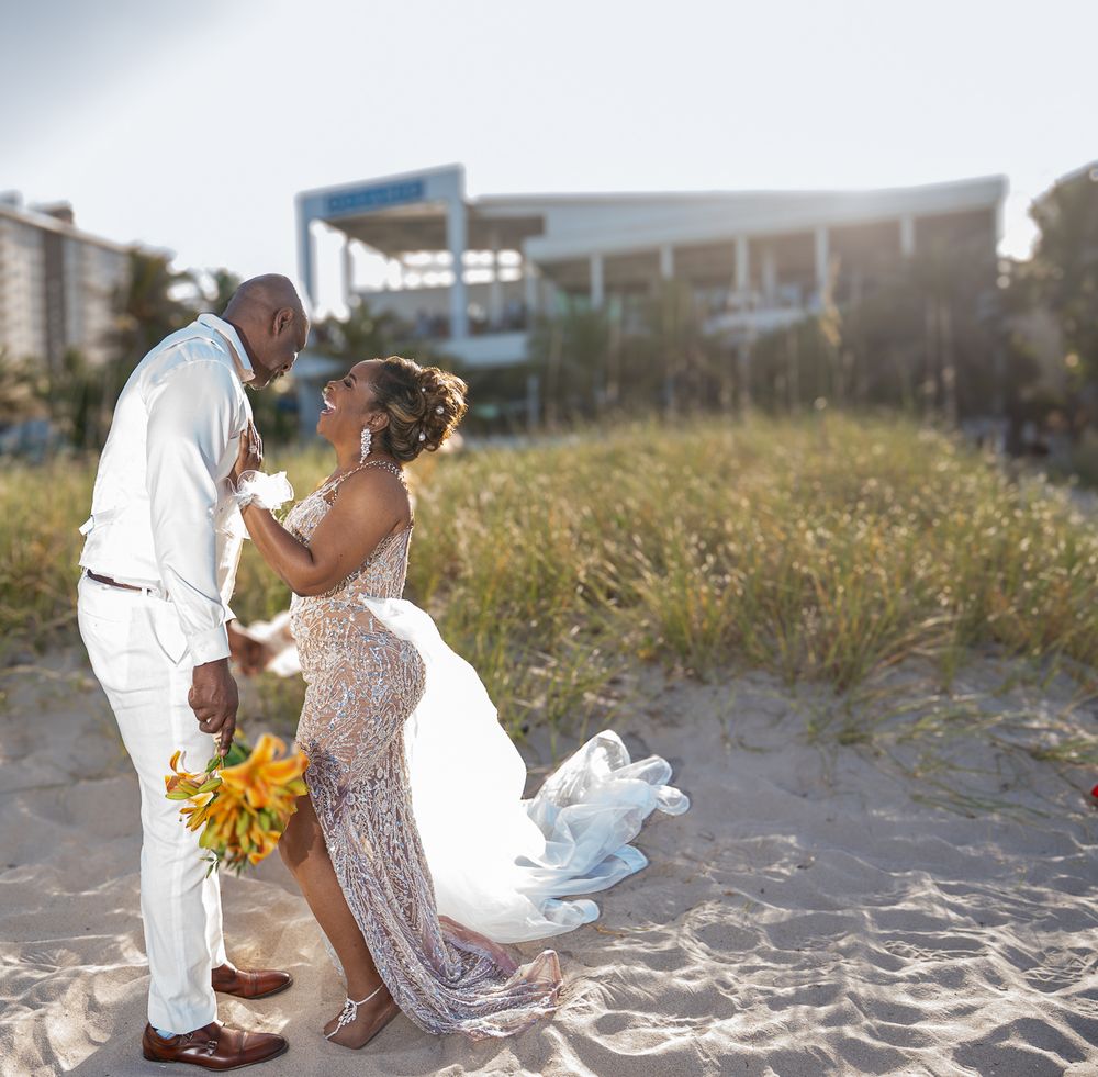 A couple shares a romantic moment on the beach during their wedding ceremony with yellow sunflowers and white attire.