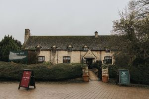 A rustic stone building with multiple wooden doors and windows set against a cloudy sky.