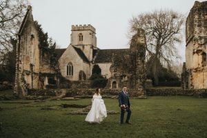 Wedding couple standing on grass in front of an old stone church with gothic architecture in winter.