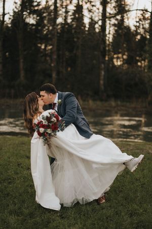 Newlyweds dance and twirl on grassy field with white wedding dress flowing in evening light.