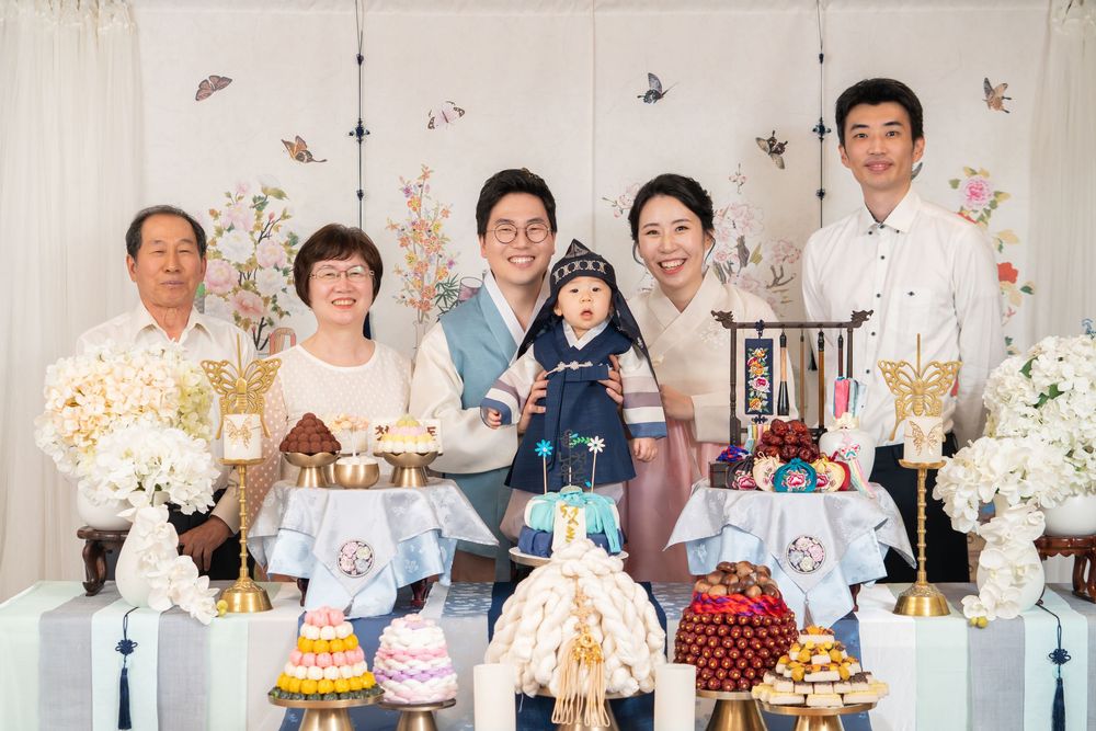 Extended family gathered around an elaborate birthday party display with cakes and decorations.