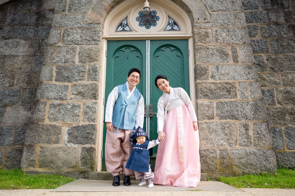 Family in traditional Korean hanbok poses in front of stone church with green doors.