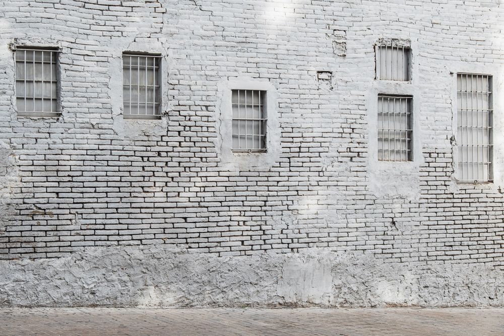 Old brick prison wall stretches across the frame with small barred windows spaced evenly along its weathered facade.