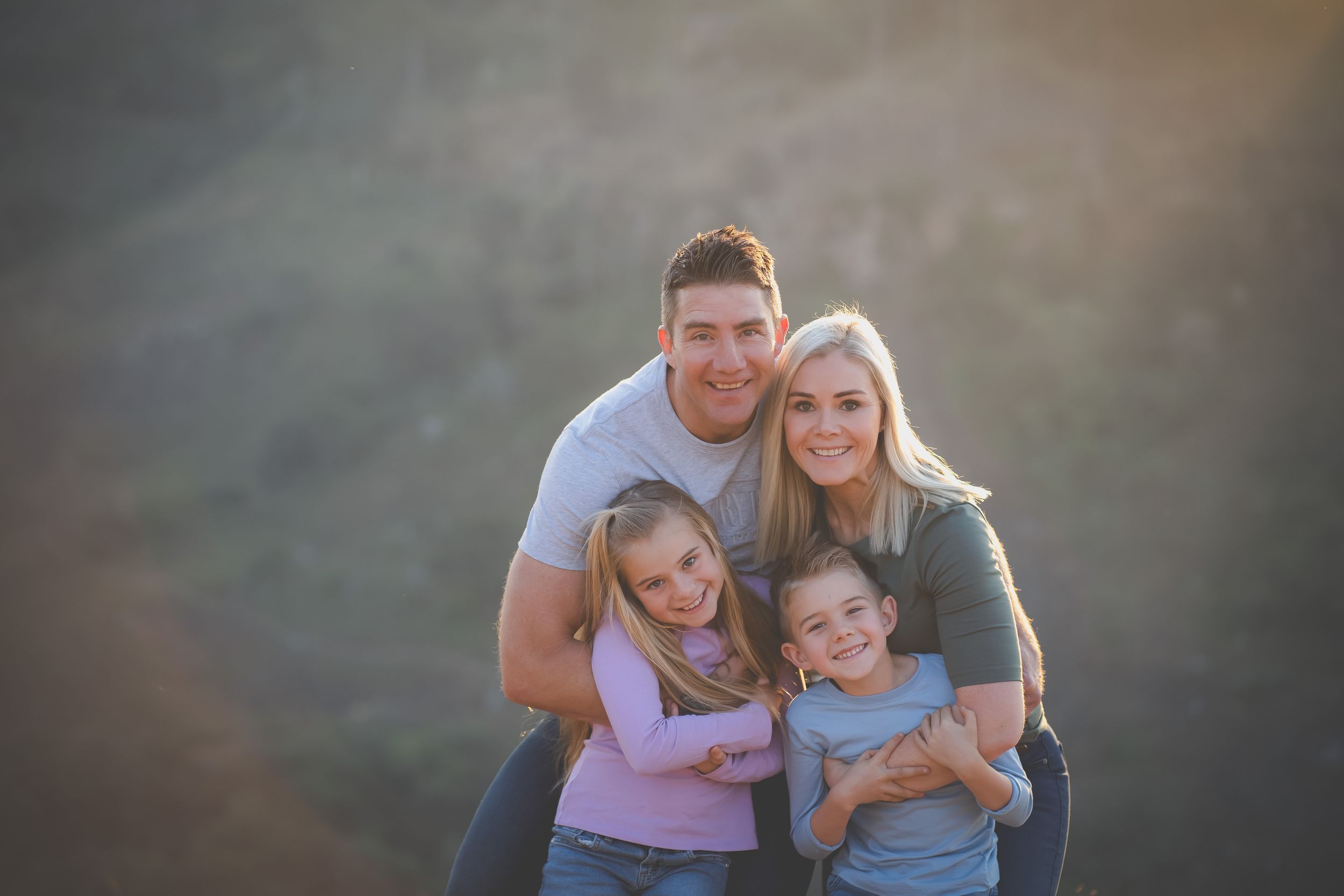 A family portrait with mom and day holding their two kids and warm sunlight on their backs
