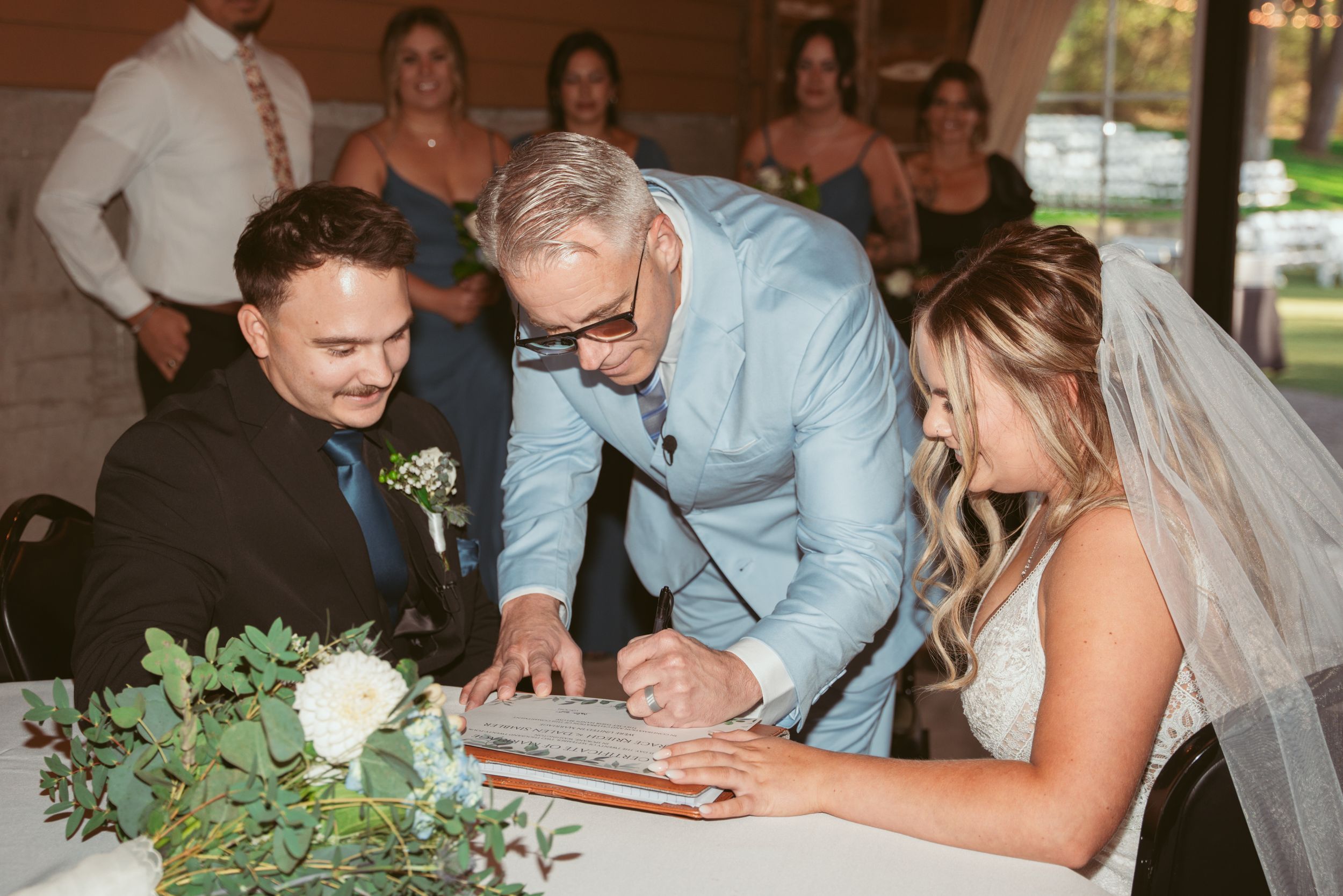 Signing of wedding documents at a ceremony decorated with white roses and greenery.
