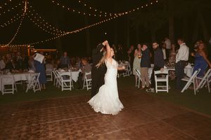 A bride in a white dress dances during her reception as guests watch from surrounding tables.