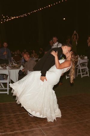 A romantic dip during a first dance on a wooden floor at an outdoor wedding reception.