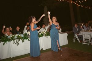 Bridesmaids in blue dresses celebrate during an outdoor evening wedding reception.