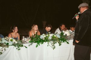Wedding reception head table decorated with lush greenery garlands and white flowers.