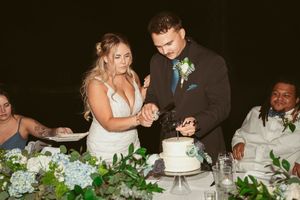 A couple cutting their white wedding cake together at an evening reception with floral decorations.