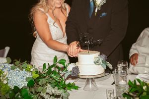 A couple cuts their elegant white wedding cake adorned with greenery and hydrangea table decorations.