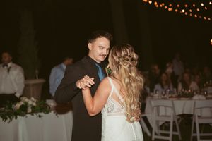 Couple shares romantic first dance at outdoor evening wedding reception with string lights overhead.