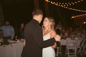 Newlyweds share their first dance at an outdoor evening reception under warm string lights.