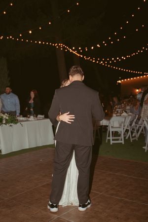 A couple dances on an outdoor dance floor under romantic string lighting at their wedding reception.