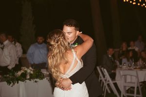 A couple shares an intimate dance at their wedding reception with romantic string lights in the background.