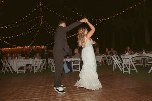 Couple sharing a playful dance move on an outdoor dance floor with string lighting overhead.