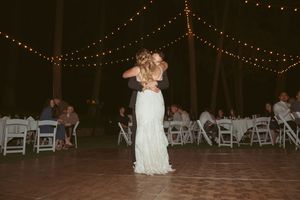 A couple dancing under strung lights at their wedding reception with white chairs in the background.