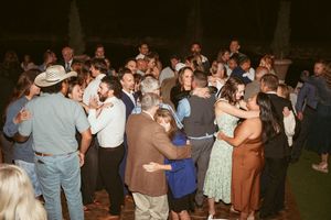 Wedding reception guests dancing together in groups on a crowded dance floor during evening celebration.