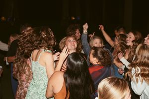 A crowd of people dancing energetically at a party with their hands in the air as hair flows in motion.