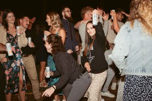 Party guests dancing and socializing at a lively indoor celebration with drinks.