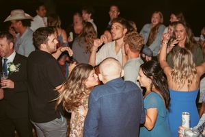 Wedding guests dancing and celebrating at a lively reception party under dim lighting.