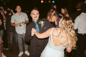 A couple dances together at their wedding reception with guests in the background.