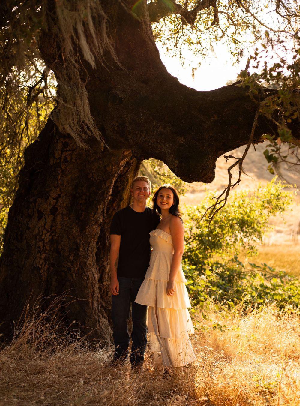 Golden sunset engagement session featuring a loving couple embracing under a majestic oak tree.
