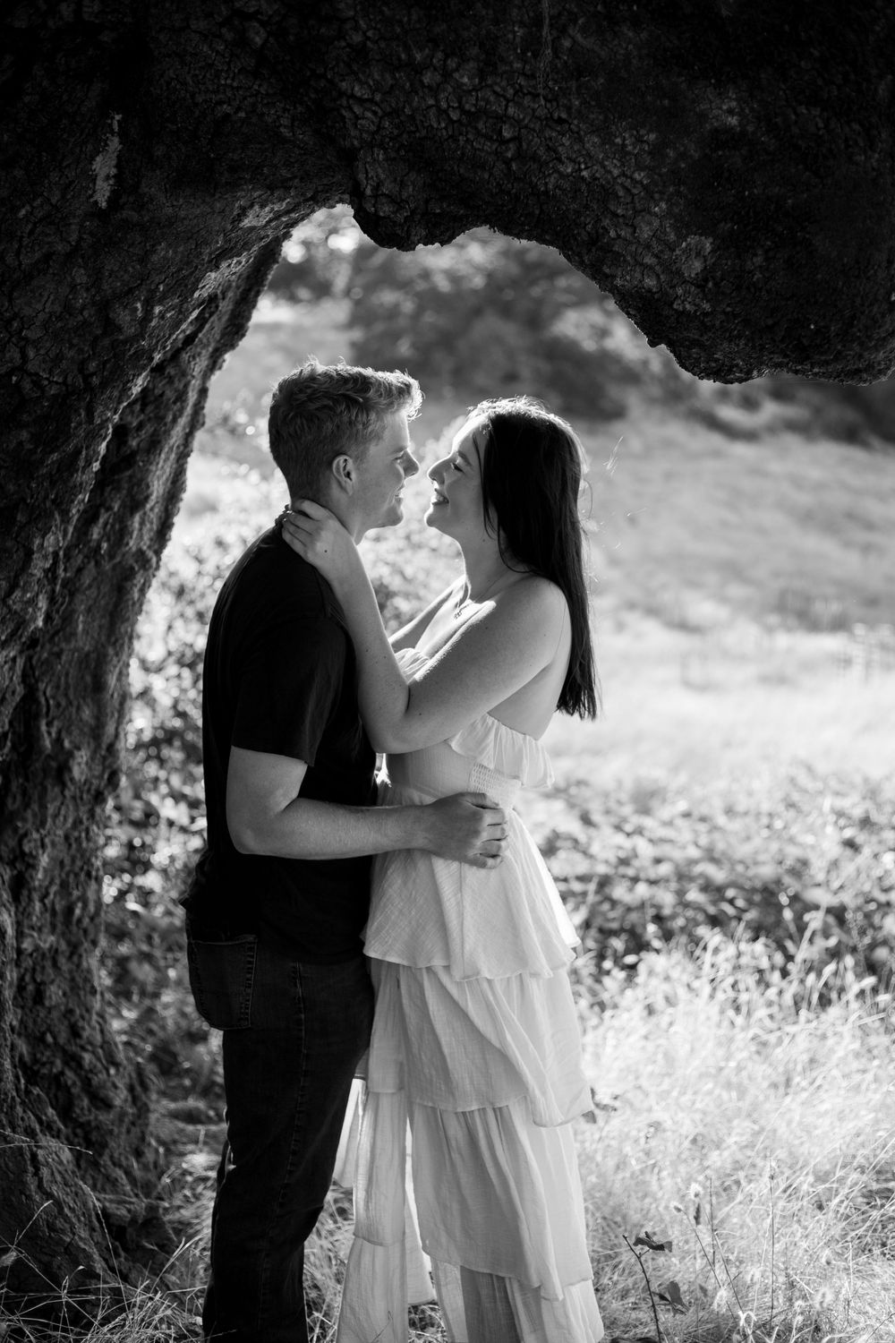 A romantic black and white portrait series of a couple sharing intimate moments beneath a tree.