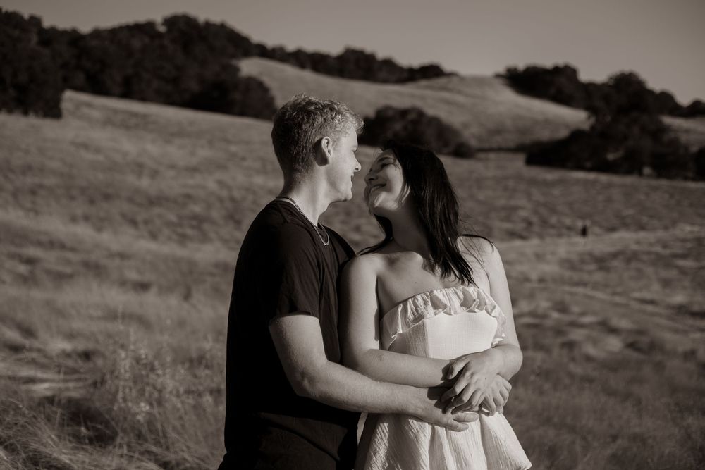 Black and white portrait of couple embracing in rolling hills landscape.