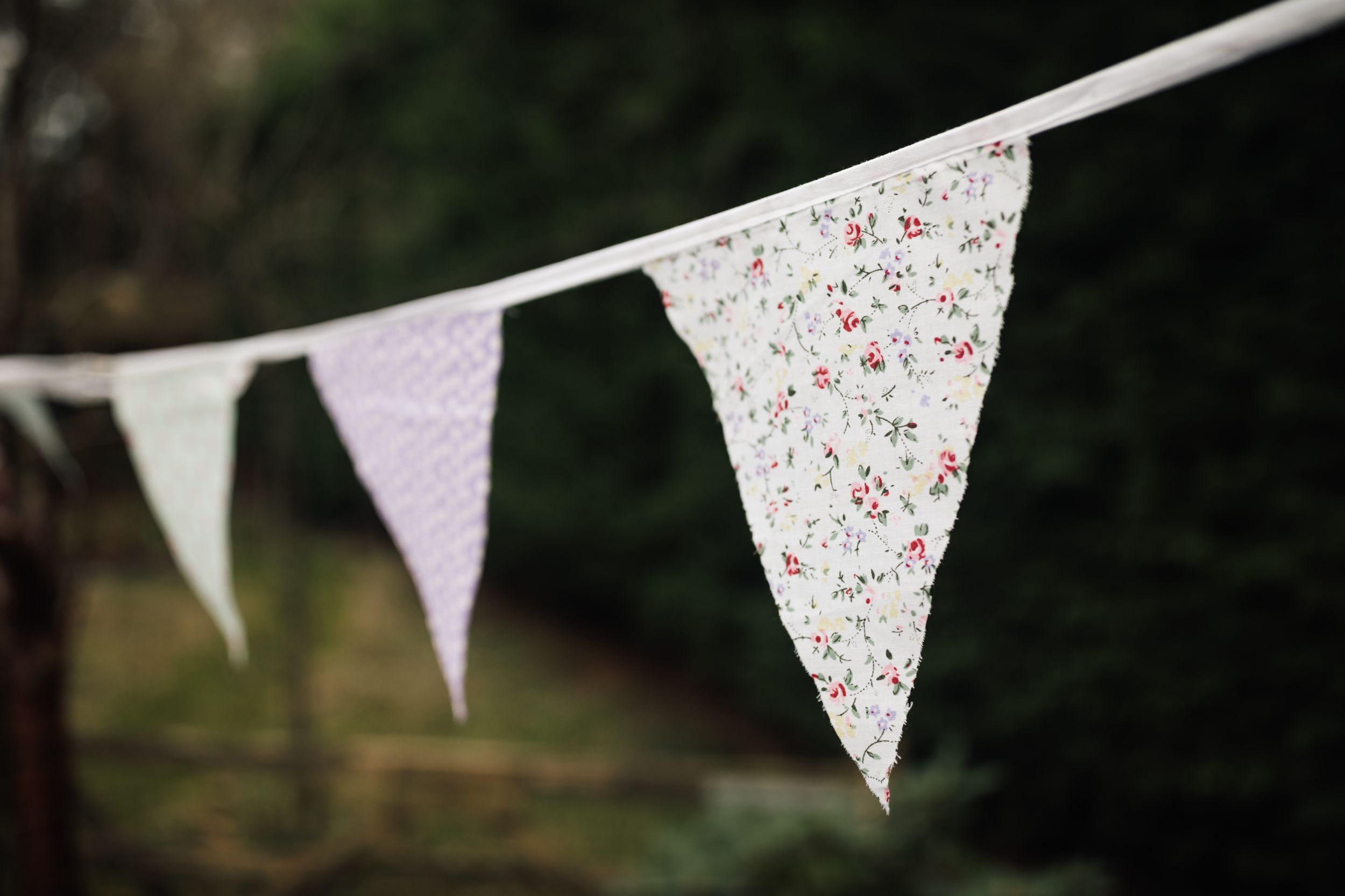 White bunting with delicate floral print decorations hangs against a dark green outdoor background.
