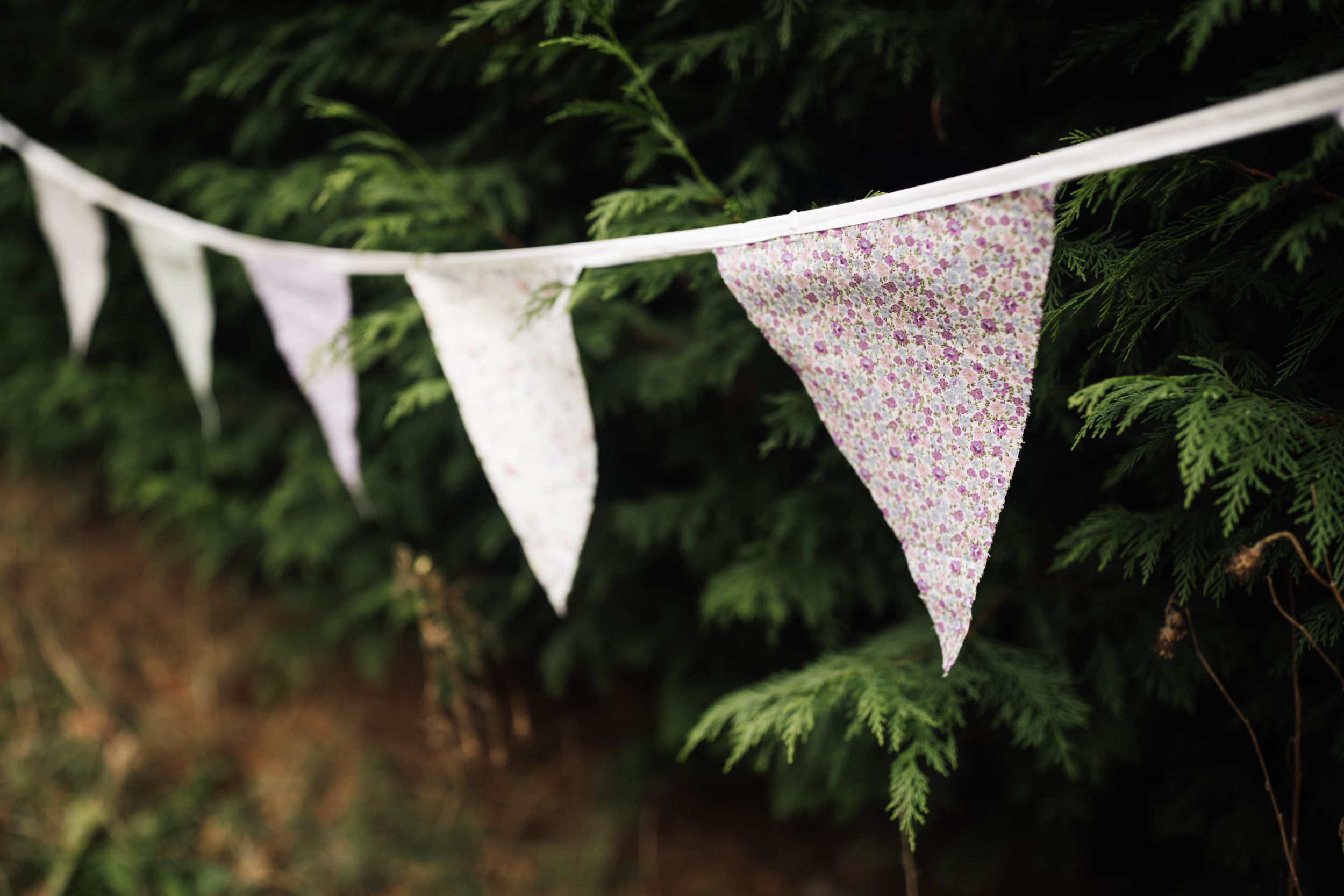 White and floral print triangle bunting flags hang against green foliage in an outdoor garden setting.