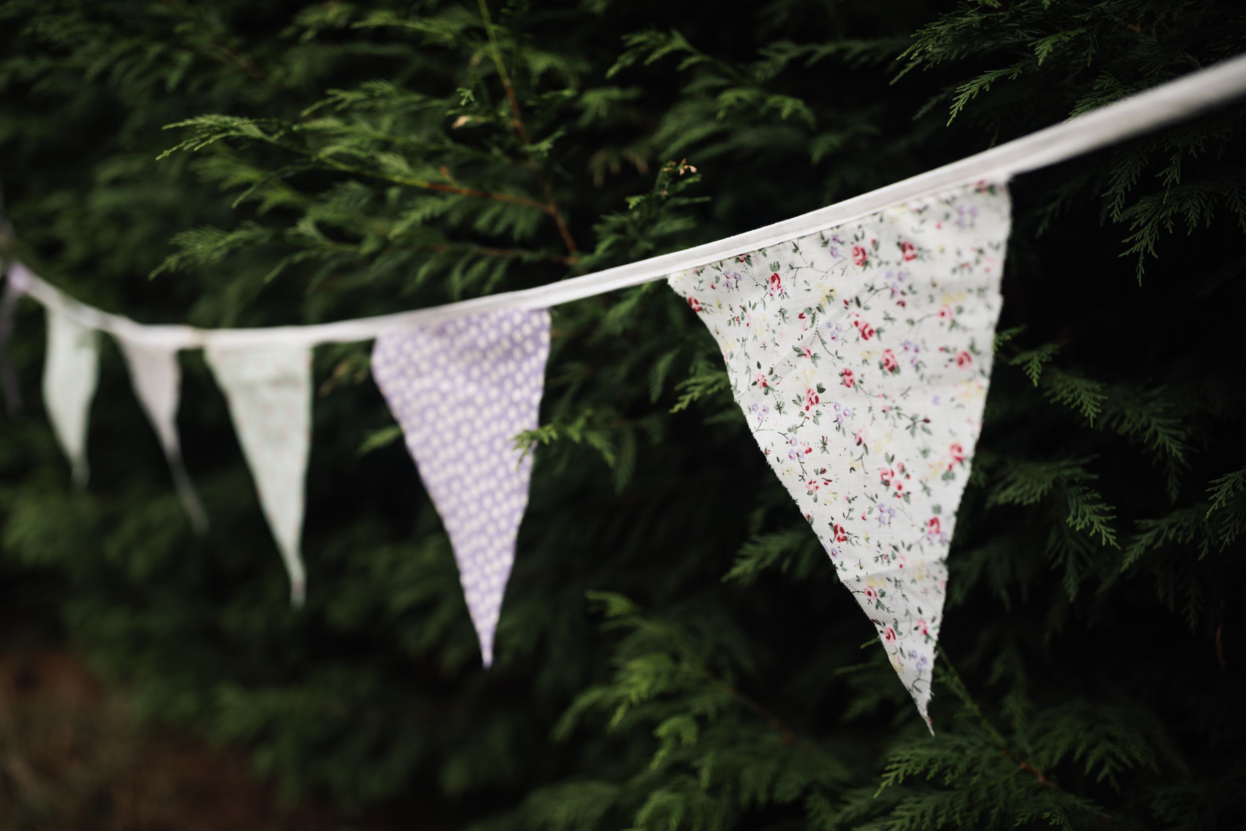 A line of decorative floral and polka dot patterned bunting flags hangs against a dark green foliage backdrop.