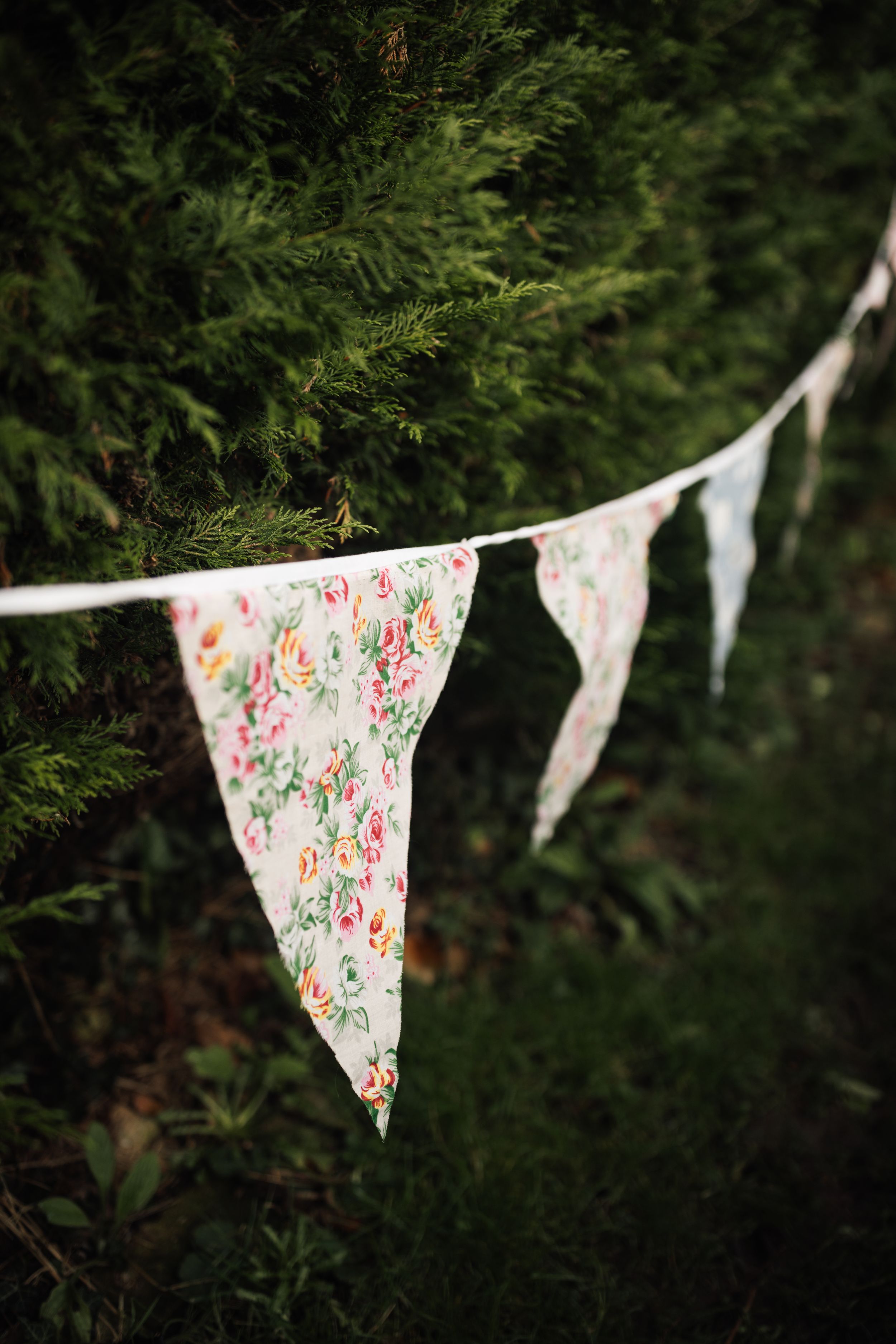 Delicate floral patterned bunting banners with pink and white designs displayed against evergreen branches.