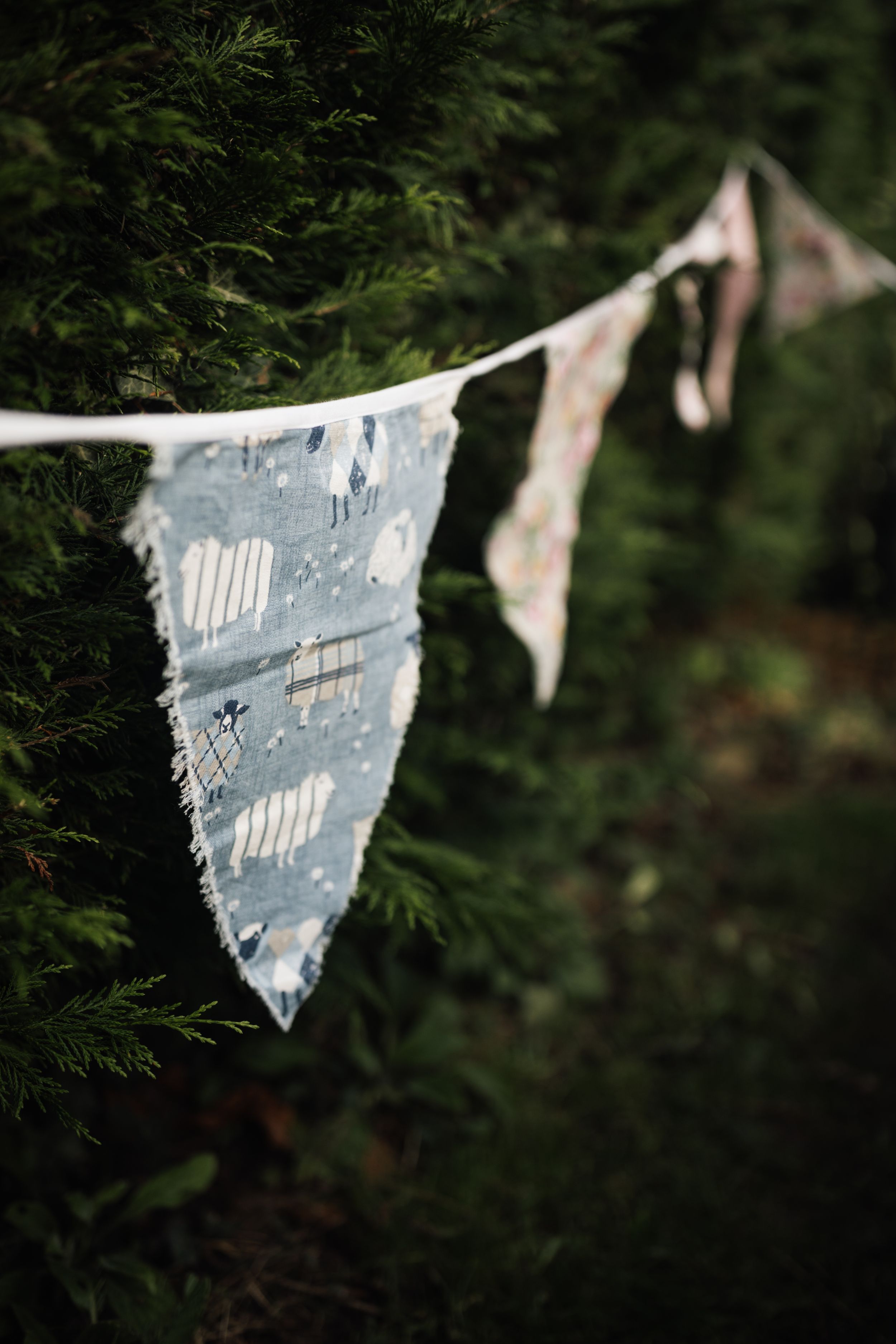A shabby blue and white decorative bunting hangs against dark green foliage in a garden setting.