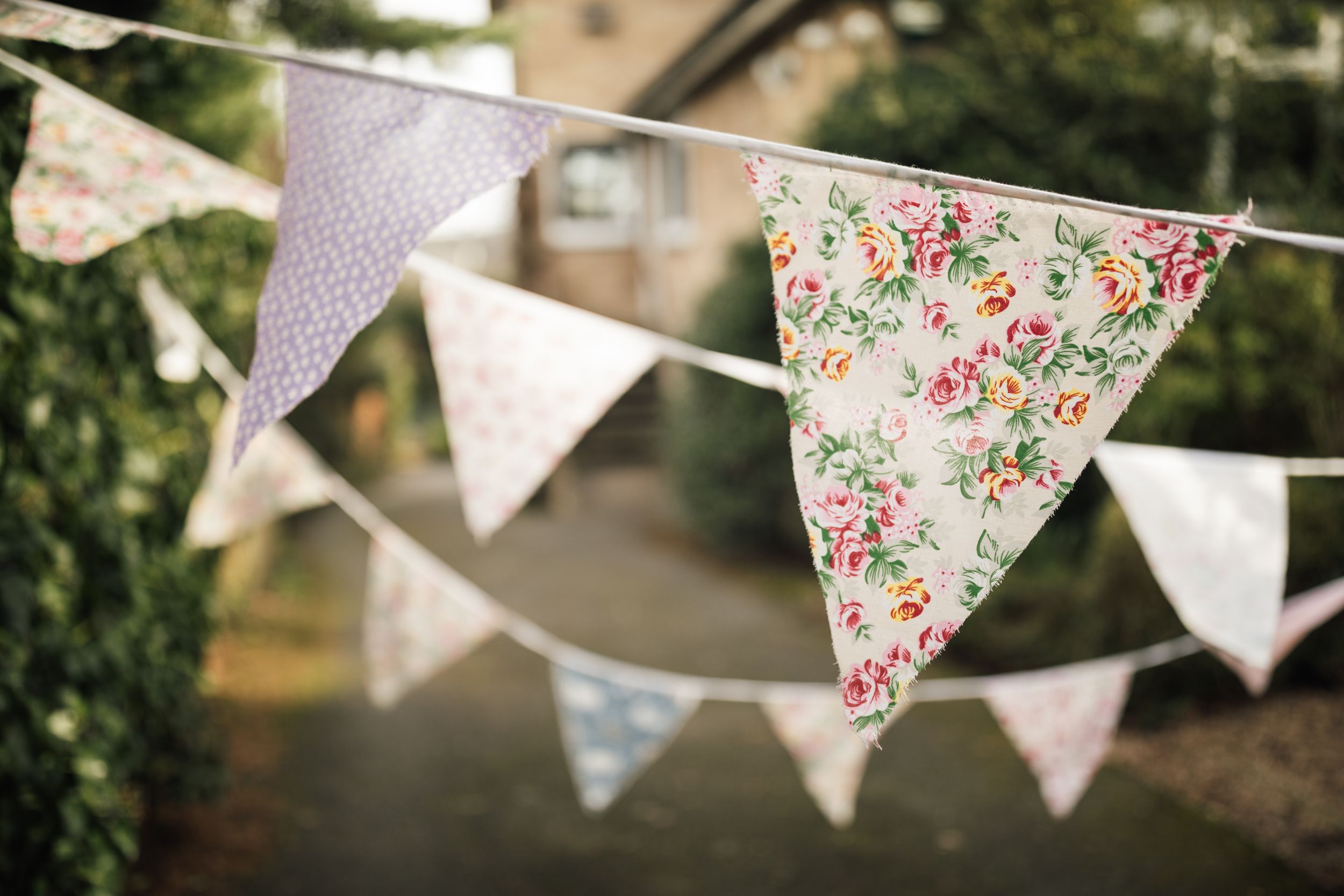 Vintage floral bunting flags with delicate pink and white patterns hang against a blurred outdoor background.