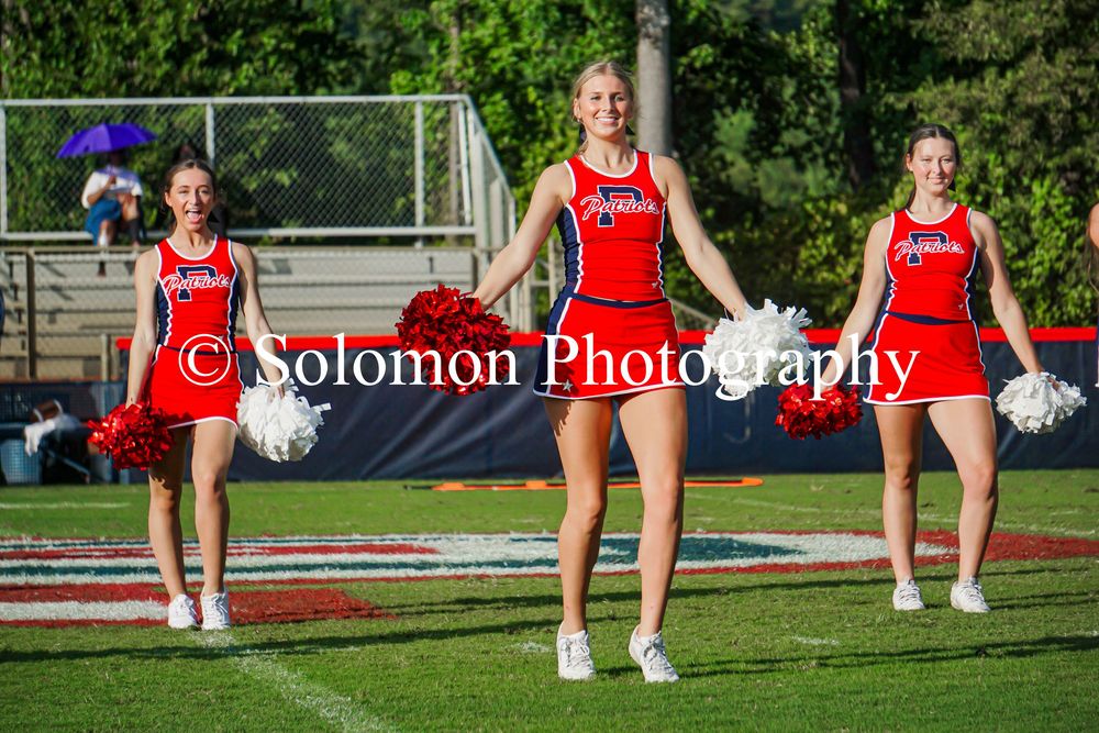 Three cheerleaders in red uniforms perform with pom-poms on football field.