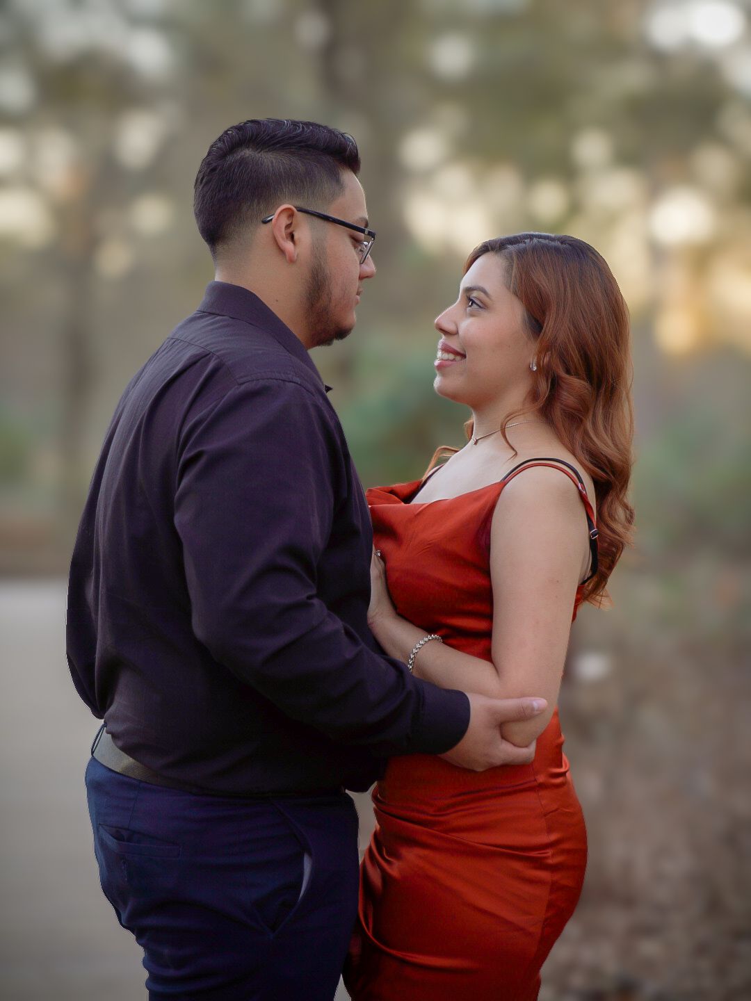 Couple in elegant red and navy attire sharing a romantic gaze outdoors at golden hour.
