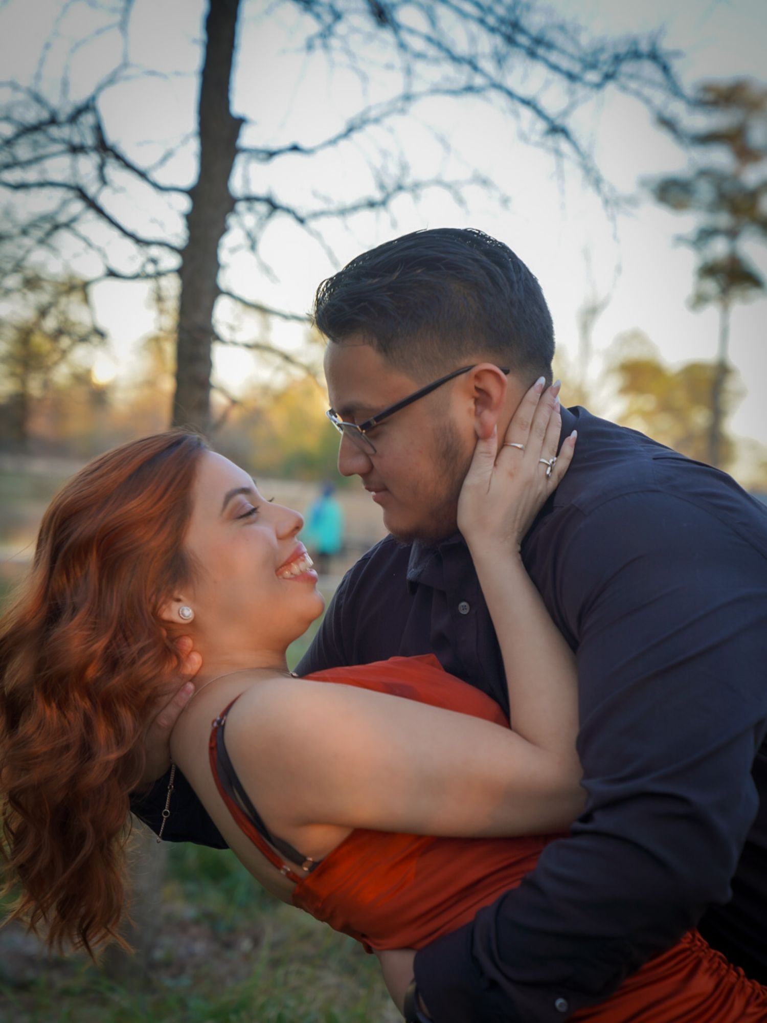 Couple in romantic embrace at sunset, woman in orange dress tenderly touching mans face outdoors.