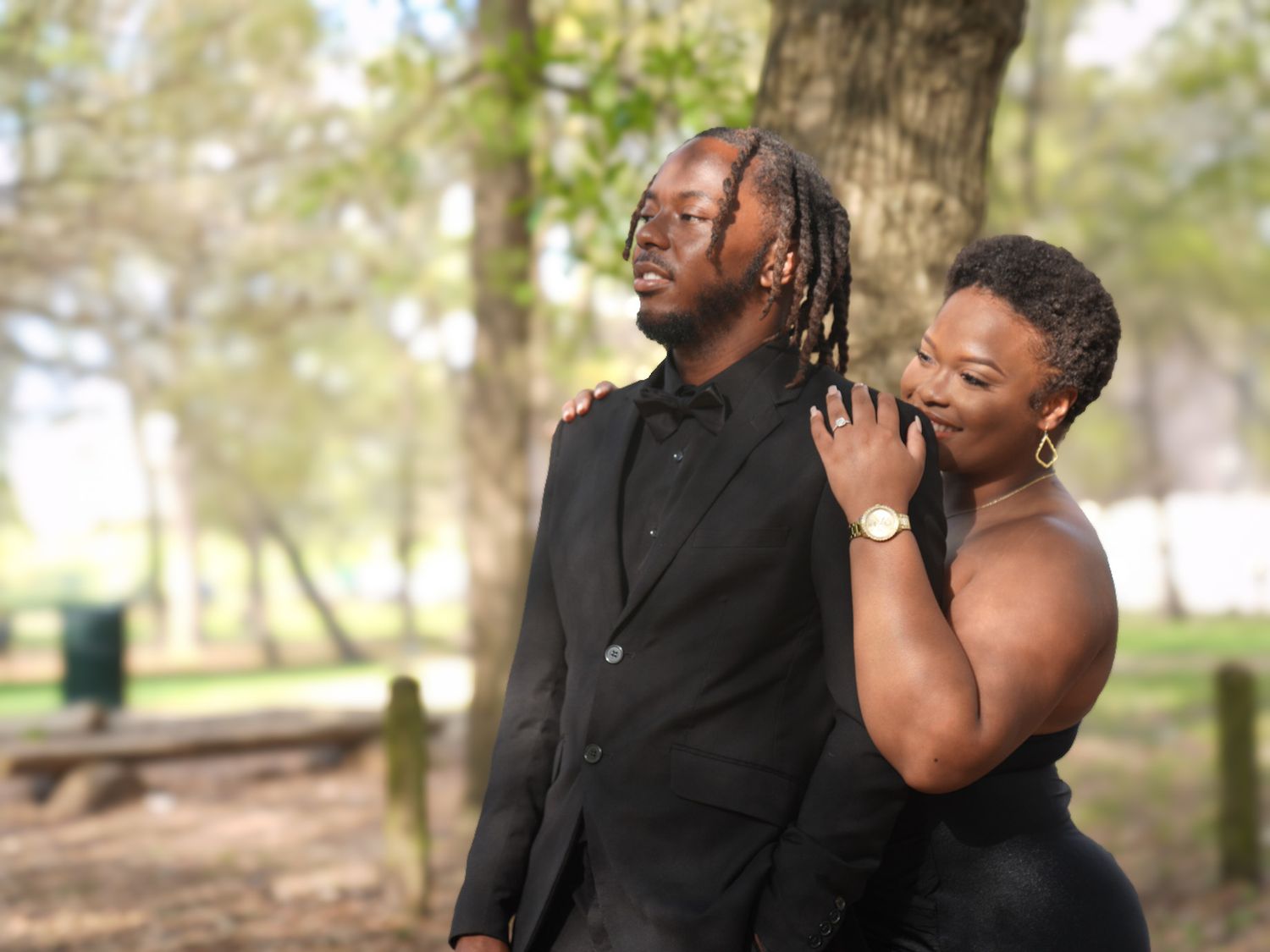 Stylish couple posing in a park, man in black suit with braids, woman in black outfit.